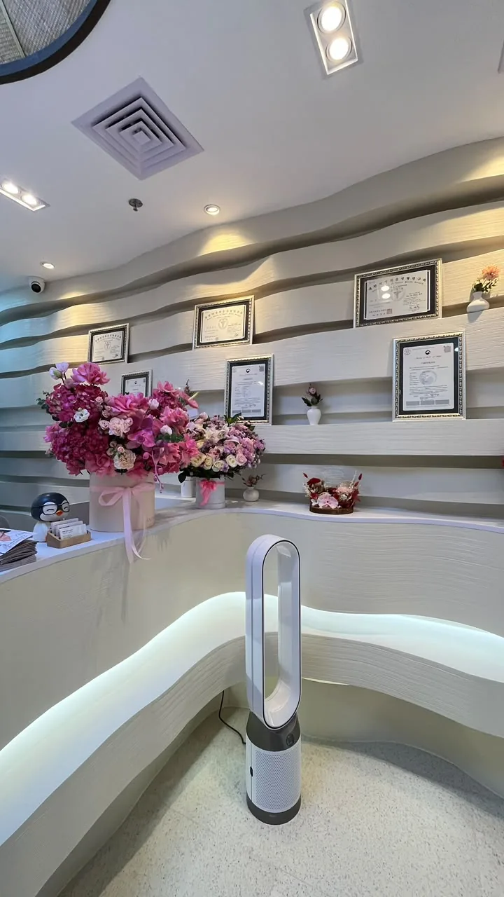 Detail area reception Hestia Women Clinic dengan meja lengkung custom, indirect lighting, display sertifikat, dekorasi floral, dan feature wall bertekstur.